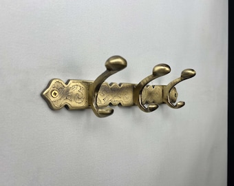 May include: A gold-toned metal coat rack with three hooks. The rack has an ornate design with a floral pattern.