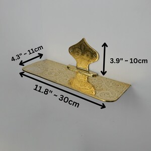 May include: A gold-colored, decorative shelf with an ornate floral design. The shelf is 11.8 inches long, 4.3 inches wide, and 3.9 inches tall. The shelf is mounted on a white wall.