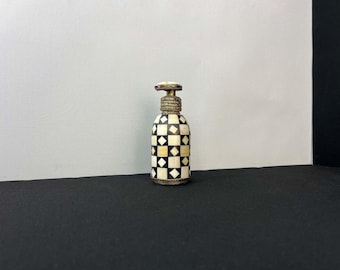 May include: A small, decorative bottle with a checkerboard pattern in black and white. The bottle has a silver top and is made of bone.