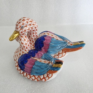 May include: A ceramic duck figurine with a white base, featuring intricate patterns in red, blue, pink, and gold. The duck's head and body are adorned with a detailed net-like design, while the wings showcase vibrant colors.