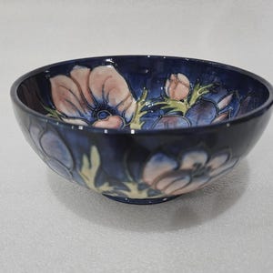 May include: A ceramic bowl with a dark blue exterior and a floral design. The interior features pink and blue flowers with green stems and leaves. The bowl has a rounded shape and a glossy finish.