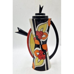 May include: A tall ceramic coffee pot featuring a black, white, yellow, and orange floral pattern. The vessel has a flared base, a slender neck, a black handle, a black spout, and a matching lid with a pointed finial. The design includes bold geometric shapes and stylised leaf motifs that wrap around the body of the pot.
