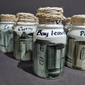 May include: Set of six ceramic spice jars with cork lids and woven straw tops. Each jar has a different label: "Salt", "Curry", "Bay Leaves", "Parsley", "Pepper", and "Oregano".