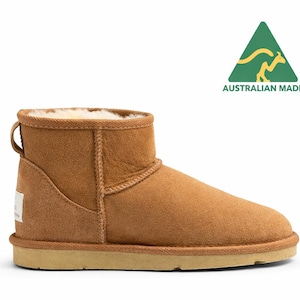 May include: A tan suede ankle boot with a thick cream-coloured wool lining and a flat beige rubber sole. A small fabric tag is visible on the heel. Above the boot, a green triangular logo features a yellow kangaroo and the text AUSTRALIAN MADE.