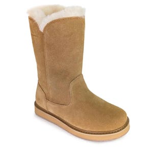 Könnte beinhalten: Ein wadenhoher Stiefel aus beigem Wildleder mit einem dicken, cremefarbenen Kunstfellfutter, das über den oberen Rand hinausragt. Der Stiefel hat eine abgerundete Zehenpartie, eine flache Sohle mit hellbraunem Rand und sichtbare Nähte an den Seiten.