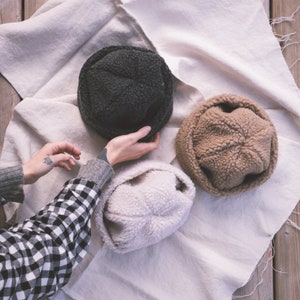 May include: Three fuzzy bucket hats in different colors: black, brown, and white. The hats are made of a soft, plush material and are perfect for keeping your head warm in the winter.