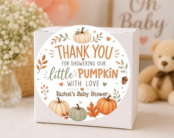May include: A round white sticker on a square white box featuring orange and green pumpkins, autumn leaves, and acorns. The text reads: THANK YOU FOR SHOWERING OUR little PUMPKIN WITH LOVE Rachel's Baby Shower, decorated with small hearts.