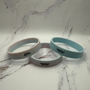 May include: Three silicone bands in the image. One is light blue, one is gray, and the other is a gradient of light blue and white. The gray band has the text "MAKERFLO 20oz Sub". The light blue band has the text "MAKERFLO 14oz Sub". The gradient band has the text "HOGG 20oz Sub".