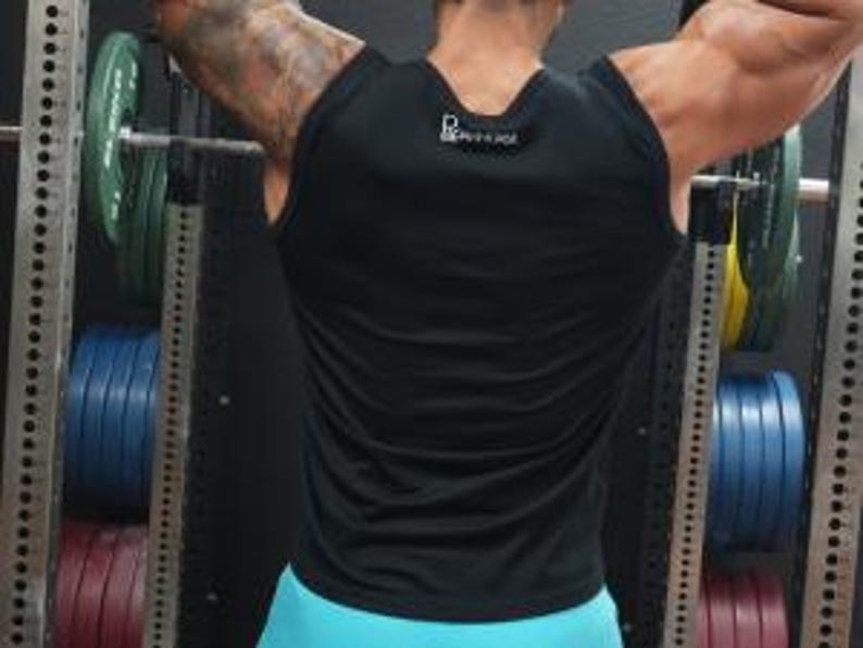 May include: A black sleeveless workout shirt with a small white logo on the upper back. The shirt is worn by a person lifting weights in a gym. The person's arms are raised, and the focus is on the shirt's design and fit.