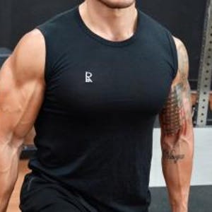 May include: Black sleeveless athletic shirt with a small white logo on the chest. The shirt is made of a lightweight material and is designed for workouts. The model is wearing the shirt in a gym setting.