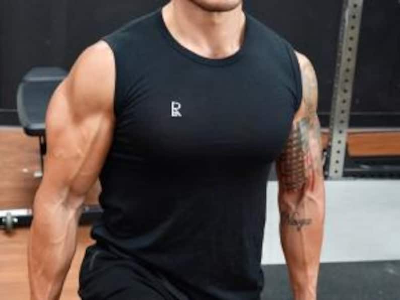 May include: Black sleeveless athletic shirt with a small white logo on the chest. The shirt is made of a lightweight material and is designed for workouts. The model is wearing the shirt in a gym setting.