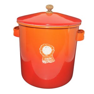 May include: A bright orange enamel stock pot with a matching lid featuring a small wooden knob handle. The cylindrical pot has two side handles and a white circular sticker on the front with the text Stock Pot printed in a stylized font.