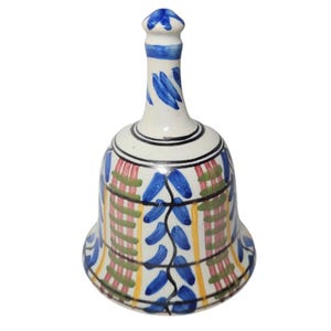May include: A ceramic bell with a white base, adorned with blue, red, green, and yellow painted patterns. The bell's handle is white with blue accents. The design features leaf-like shapes and vertical stripes, creating a decorative piece.