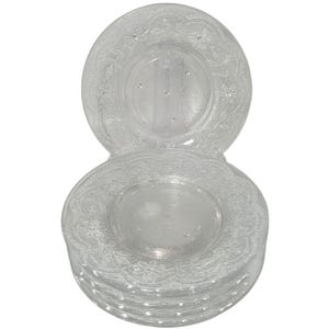 May include: A stack of clear glass plates featuring a raised, textured floral and lace-like pattern along the scalloped rims. The center of each plate is smooth and transparent, while the edges display intricate embossed botanical details.