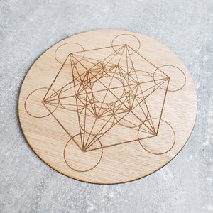 May include: A round wooden coaster featuring a geometric design of a star with overlapping circles. The design is laser engraved into the wood.