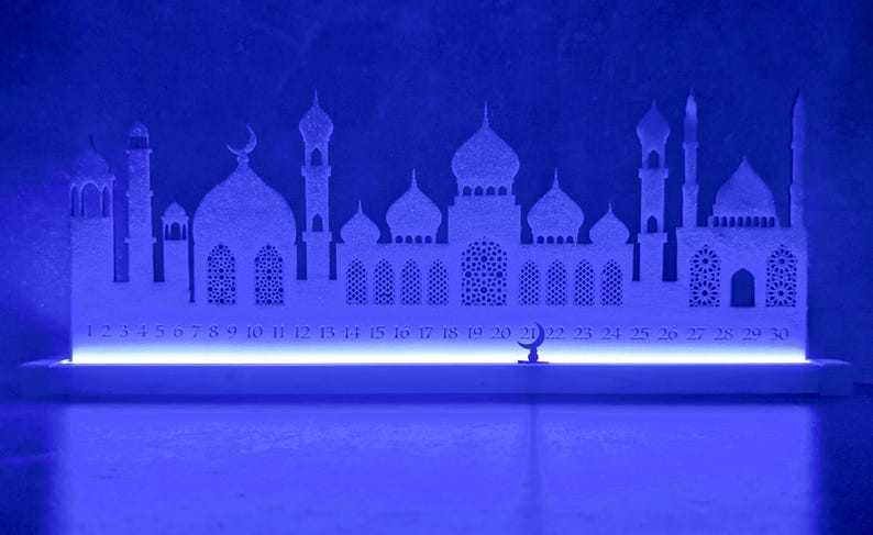 May include: White silhouette of a mosque with a blue LED light strip at the base. The silhouette includes a crescent moon and numbers 1 through 30.