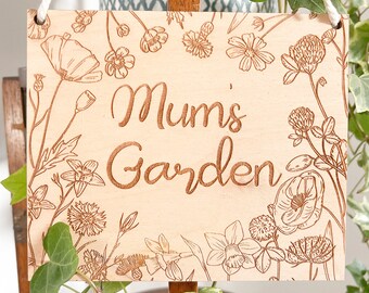Könnte beinhalten: Ein Holzschild mit einem Blumendesign und dem Text "Mum's Garden" in brauner Farbe.