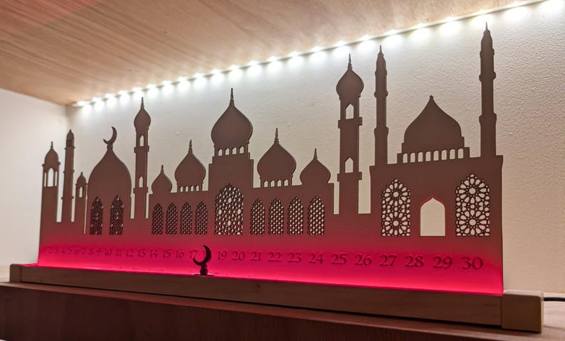 May include: A wooden Ramadan advent calendar with a silhouette of a mosque and a crescent moon. The calendar has numbers 1-30 on the bottom and is lit with red LED lights.