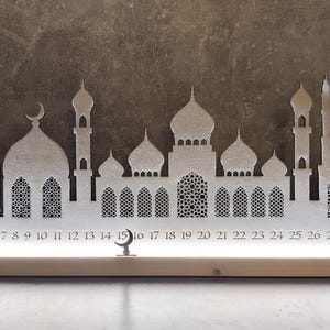 May include: White wooden Ramadan advent calendar with a silhouette of a mosque and crescent moon. The calendar has 30 numbered windows, 1-30.