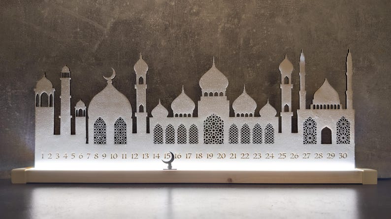 May include: White wooden Ramadan advent calendar with a silhouette of a mosque and crescent moon. The calendar has 30 numbered windows, 1-30.