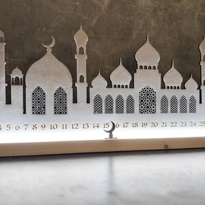 May include: White wooden Ramadan calendar with a silhouette of a mosque and crescent moon. The calendar features numbers 1 through 30.