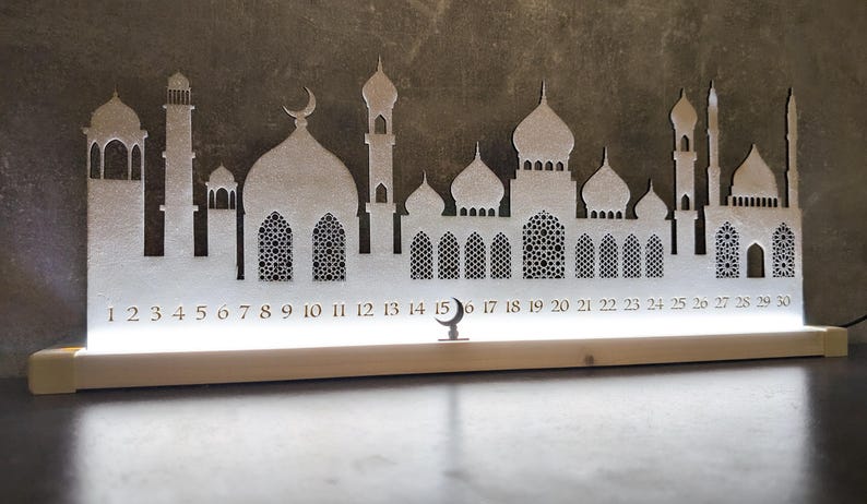 May include: White wooden Ramadan calendar with a silhouette of a mosque and crescent moon. The calendar features numbers 1 through 30.