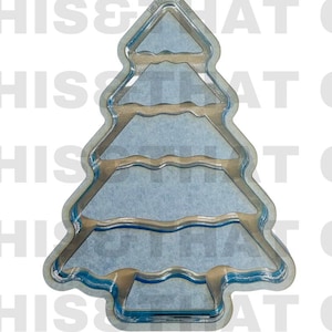 May include: A clear, stackable Christmas tree-shaped mold with a multi-tiered design. The mold features distinct horizontal sections that create a layered tree silhouette. The text STACKABLE Christmas Tree is visible at the top of the image.