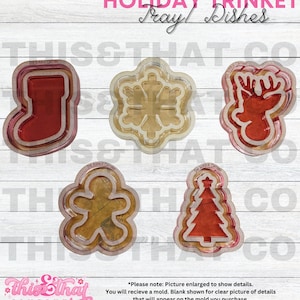 Puede incluir: Cinco moldes de plástico transparente para hacer manualidades de resina. Los moldes tienen forma de calcetín, copo de nieve, reno, hombre de jengibre y árbol de Navidad. Los moldes están superpuestos, con la capa superior mostrando el producto de resina terminado. El texto "Holiday Trinket Tray/Dishes" está en la parte superior de la imagen.