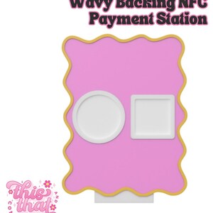 May include: A pink NFC payment station with a wavy gold border. The station has a circular and a square white holder. The text "Wavy Backing NFC Payment Station" is at the top. The logo "this that company" is at the bottom left.
