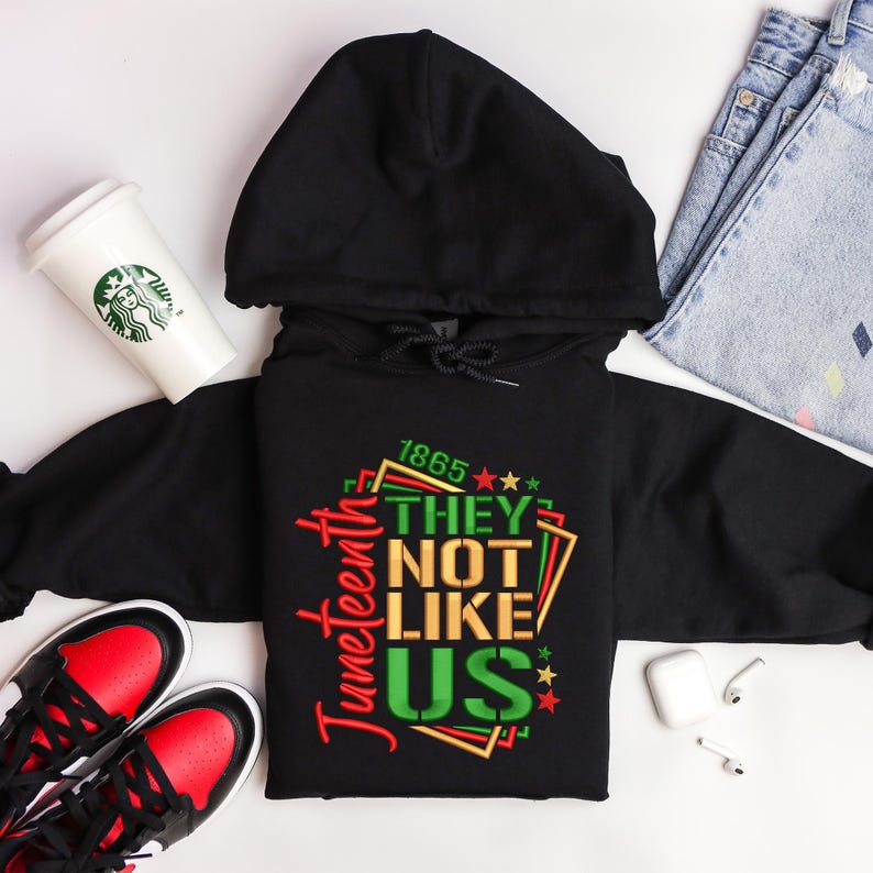May include: Black hoodie with a red, green, and gold graphic that says "Juneteenth 1865 They Not Like Us" with stars.