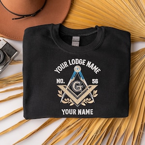 May include: Black crewneck sweatshirt with a Masonic emblem design. The emblem features a compass, square, and the letter "G" in the center, with text that reads "Your Lodge Name", "No. 56", and "Your Name".