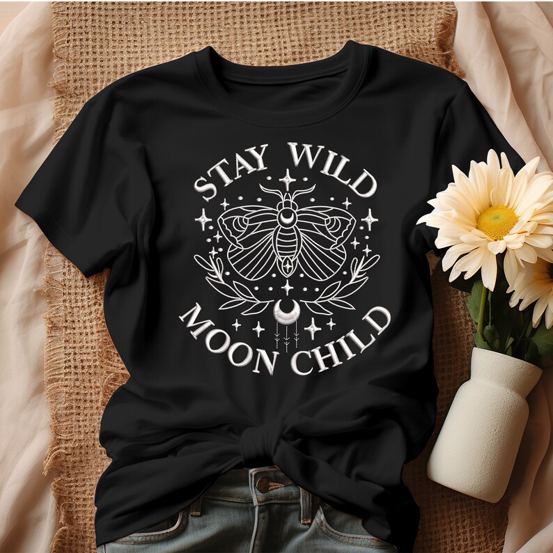 Puede incluir: Camiseta negra con un dise&ntilde;o gr&aacute;fico blanco que presenta una polilla, estrellas y el texto "Stay Wild Moon Child".