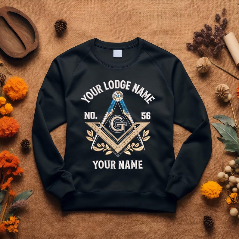 May include: Black sweatshirt featuring a Masonic emblem with the text "YOUR LODGE NAME" above and "YOUR NAME" below. The emblem includes a compass, square, and the letter "G". The number "56" is also displayed.