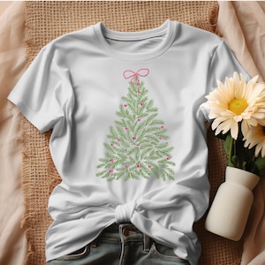 May include: White t-shirt featuring an embroidered Christmas tree design. The tree is green with pink ornaments and a pink bow at the top. The shirt is made of a soft material and is perfect for the holiday season.