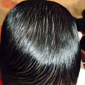 Puede incluir: Primer plano de la cabeza de una persona con cabello negro peinado hacia atr&aacute;s, liso y brillante.