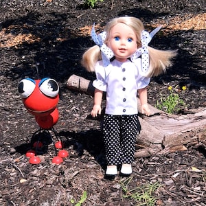 May include: A doll with blonde hair and blue eyes, wearing a white blouse with black buttons and black and white polka dot pants. A red metal ant sculpture with large eyes stands nearby. The doll has white and black polka dot bows in her hair.