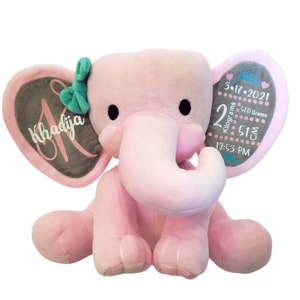 May include: Pink plush elephant stuffed animal with gray ears. The ears have embroidered details including the name Khadija, the date 3-17-2021, 2 kilograms, 570 grams, 51 cm, and 12:53 PM.