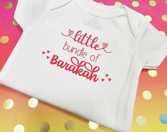 May include: White baby onesie with red text that reads "little bundle of Barakah" with hearts around the text.