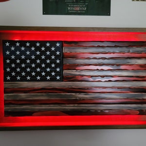 May include: A wooden American flag with red, white, and blue paint, mounted in a dark wood frame with red LED lights around the perimeter.