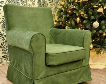 May include: An armchair upholstered in solid olive green fabric with a smooth, matte texture. The chair features rounded armrests, a thick removable seat cushion, and a skirted base with piping details along the seams of the frame and cushion.