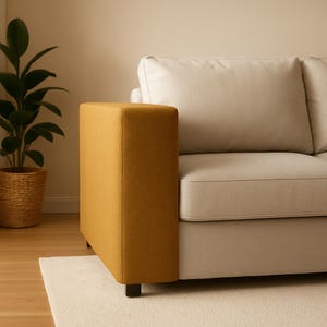 May include: A modern sectional sofa with a mustard-colored armrest and light beige cushions. The sofa sits on a white rug and has a potted plant in the background. The armrest is a solid, rectangular shape.