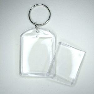 May include: A clear plastic keychain with a rectangular frame for a photo or other small item. The keychain has a silver metal ring.