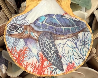 May include: A decorated scallop shell with a sea turtle design. The turtle's shell is blue and purple, with a detailed head and flippers. The background features coral and sea plants, with a gold-painted edge.