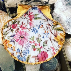May include: A white seashell with a gold trim and a floral pattern. The shell is decorated with pink, red, blue, and yellow flowers.