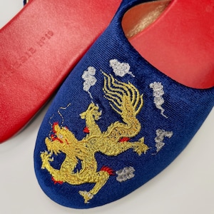 May include: A pair of blue velvet slippers with a gold embroidered dragon design. The slippers have red soles.