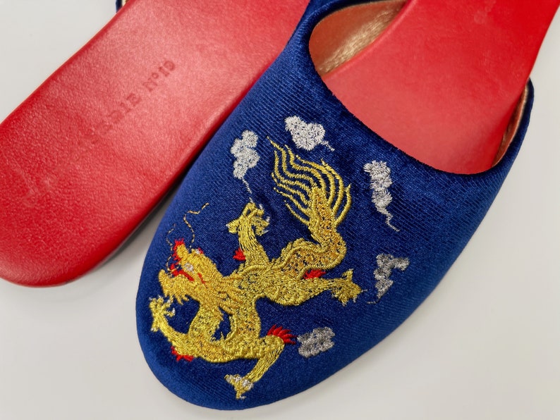 May include: A pair of blue velvet slippers with a gold embroidered dragon design. The slippers have red soles.