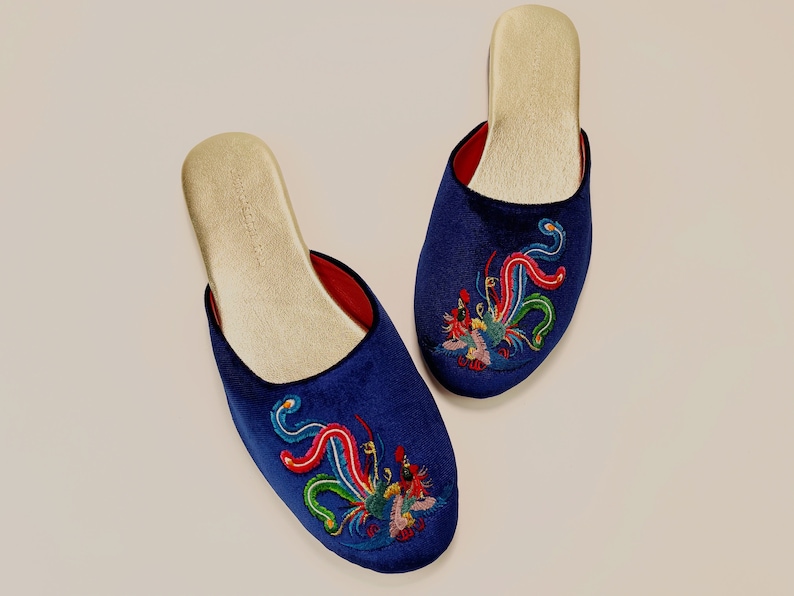 May include: A pair of blue velvet slippers with embroidered colorful phoenix designs. The slippers have a gold lining.