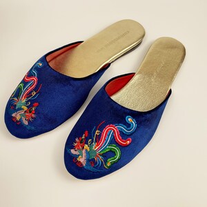 May include: A pair of blue velvet slippers with embroidered phoenix designs in red, green, and yellow. The slippers have a gold insole.