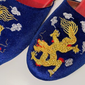 May include: A pair of blue velvet slippers with gold embroidered dragons and white clouds. The slippers have red trim around the edges.