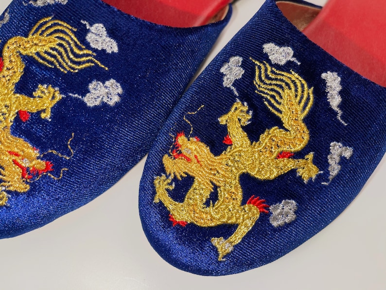 May include: A pair of blue velvet slippers with gold embroidered dragons and white clouds. The slippers have red trim around the edges.
